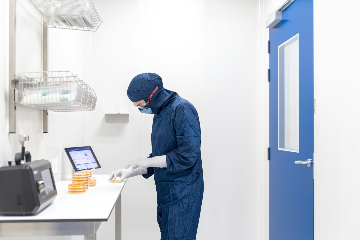 Técnico con traje azul examina placas de Petri en laboratorio.