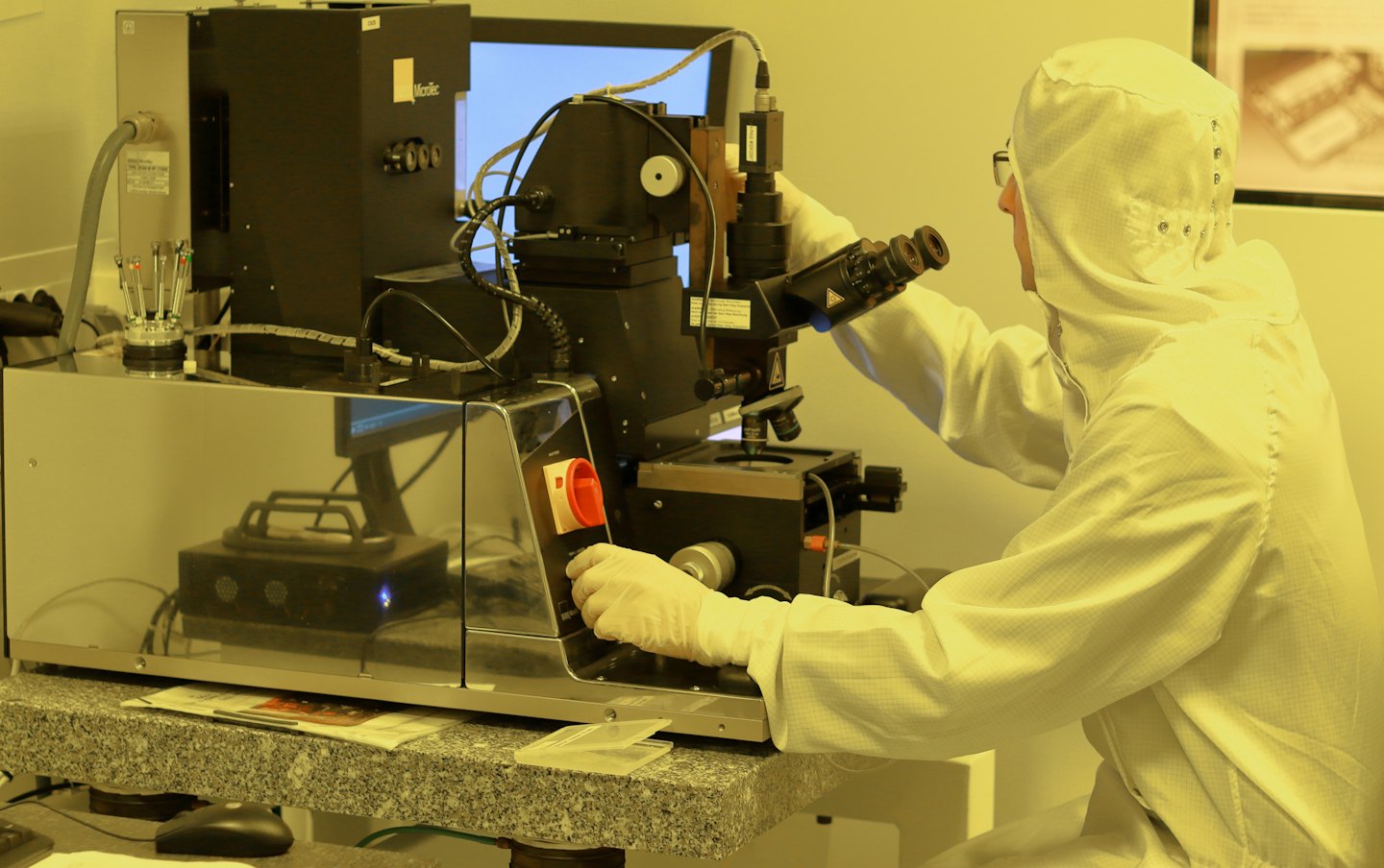 Científico con traje de sala limpia operando un instrumento complejo con microscopio.
